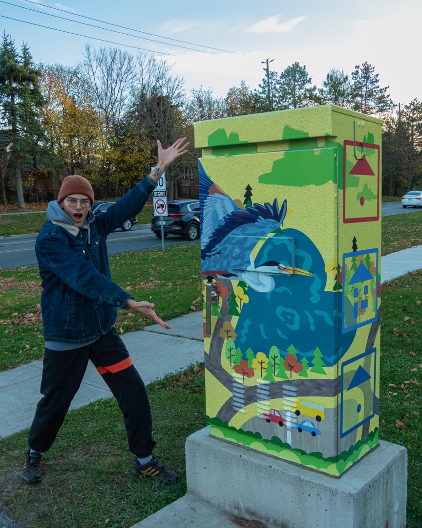 The artist posing next to his mural on a traffic light box.